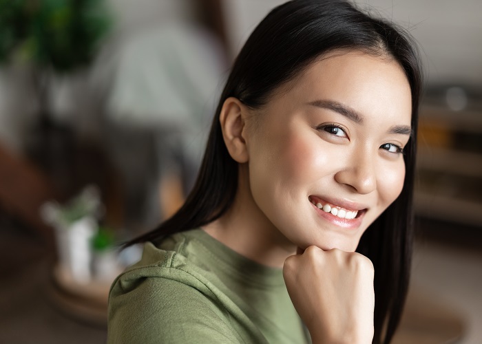 Portrait of young asian woman with clean glowing skin, looking and smiling at camera, sitting at home alone in living room. Lifestyle concept Portrait of young asian woman with clean glowing skin, looking and smiling at camera, sitting at home alone in living room. Lifestyle concept