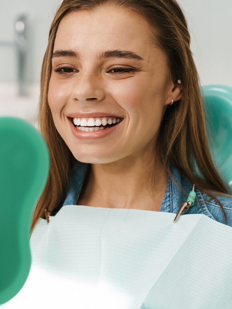 Young woman smiling while examining her teeth in a mirror after a cleaning at a dental clinic