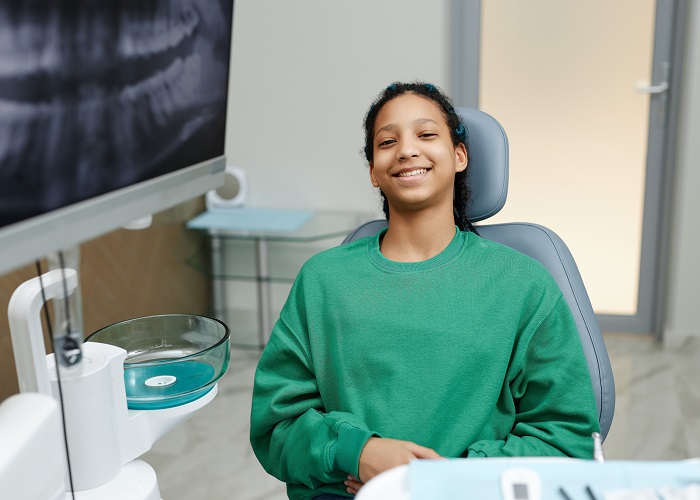 Black teenage girl sitting in dental chair and smiling at camera